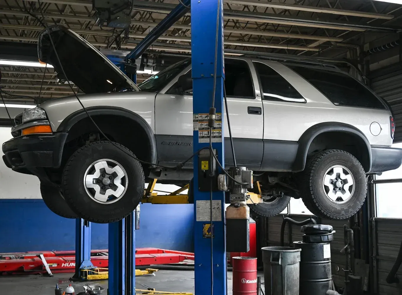 Silver SUV lifted on a hydraulic car repair hoist in an auto shop, hood open. | Jones Complete Car Care