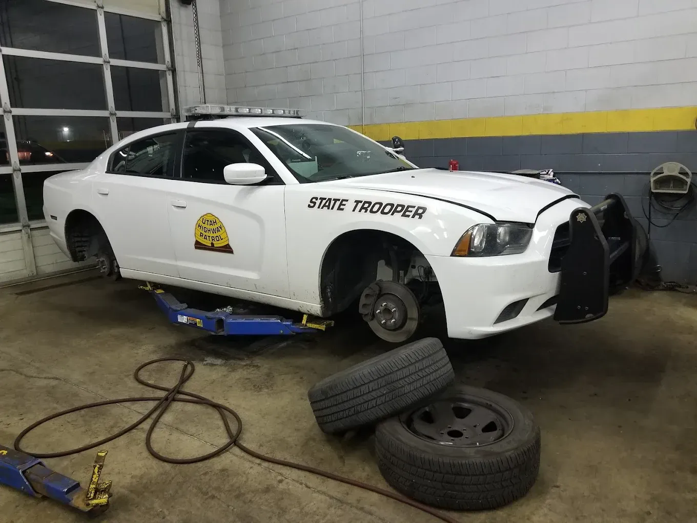 White race car in a garage, raised on a jack with wheels removed and tools on the floor. | Jones Complete Car Care