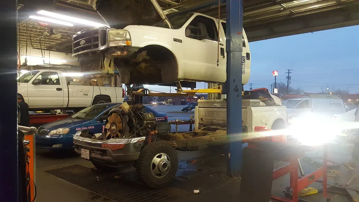 Auto repair shop with a lifted white car over a blue pickup under bright shop lights. | Jones Complete Car Care