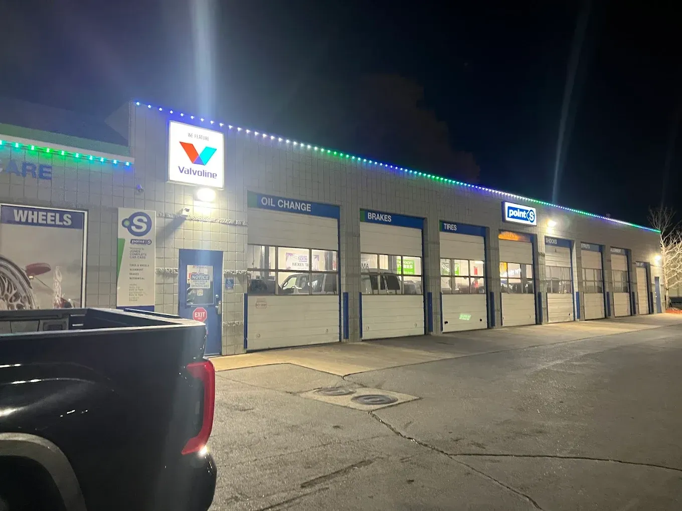 Nighttime exterior of an auto repair shop with lit bays and a black truck in the foreground | Jones Complete Car Care