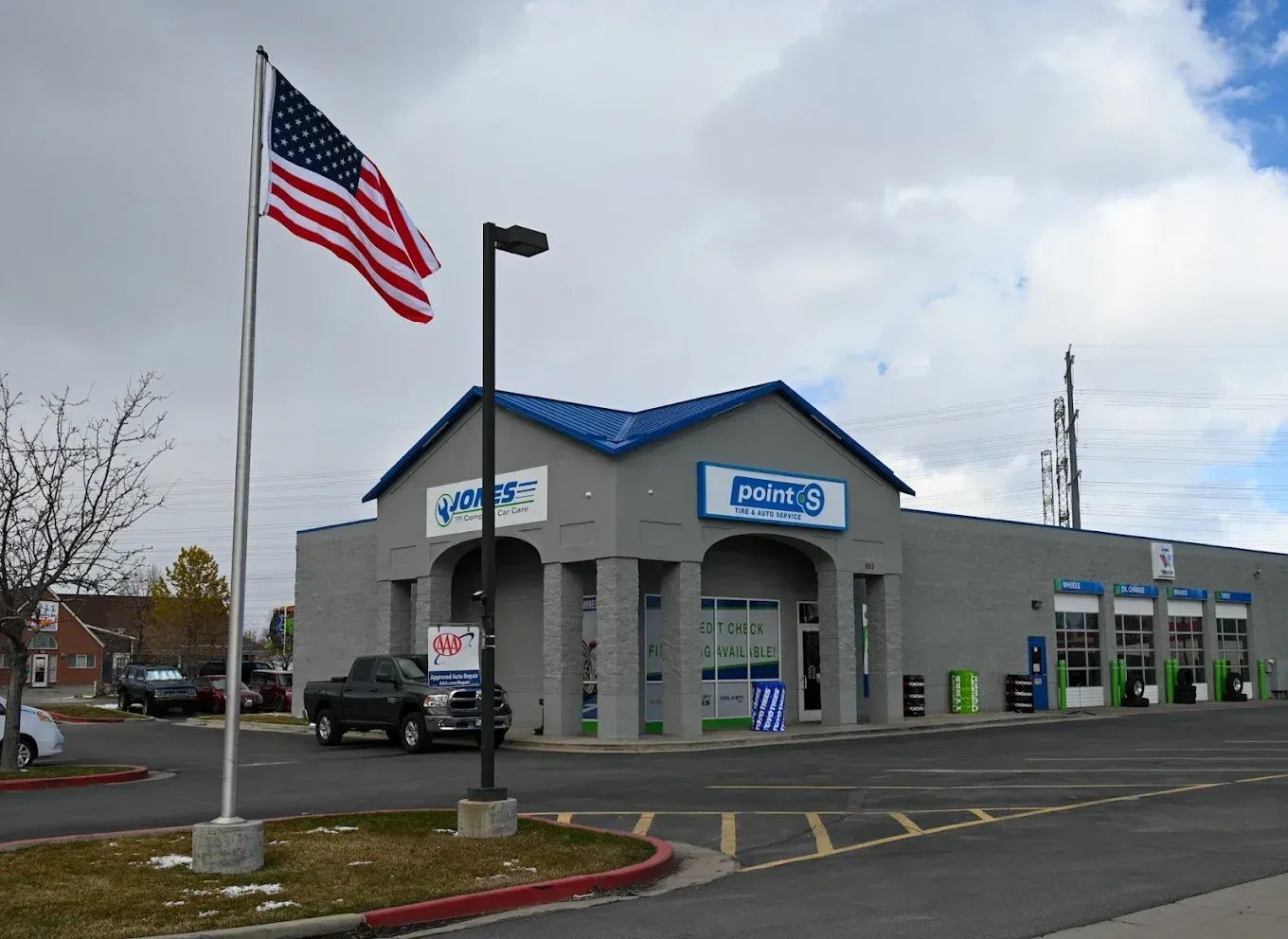 American flag in front of a gray auto repair shop with blue roof trim and sign at a street corner | Jones Complete Car Care