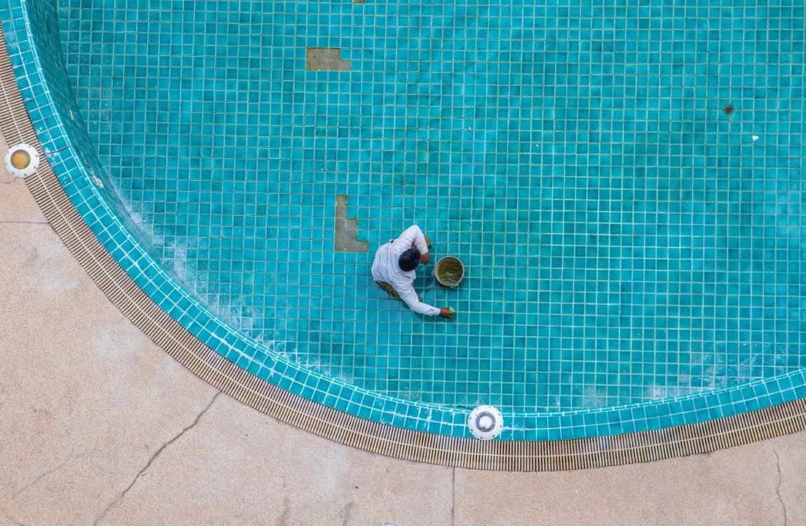 A man is cleaning a swimming pool with a bucket.