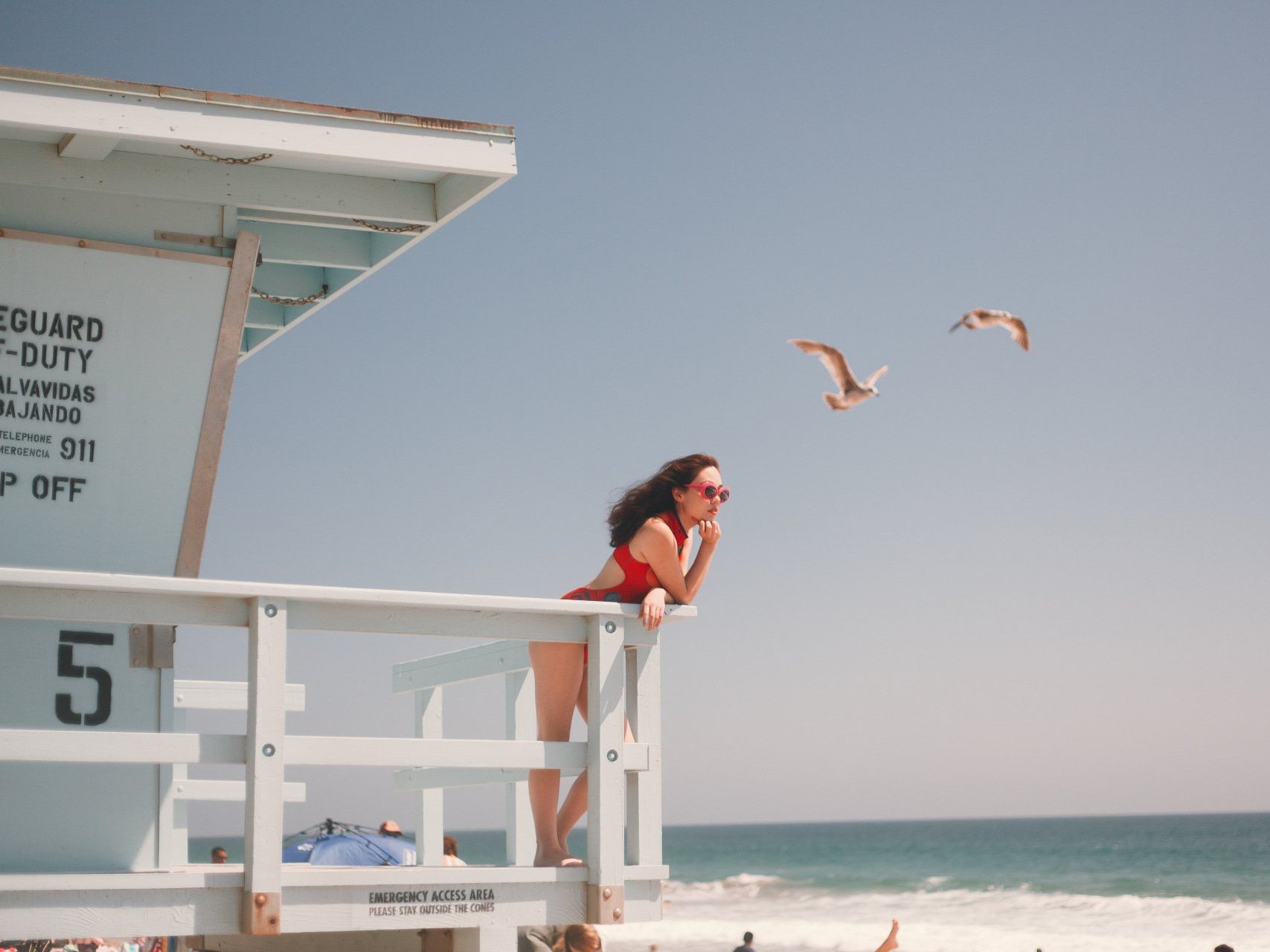 A woman stands on a lifeguard tower looking out over the ocean