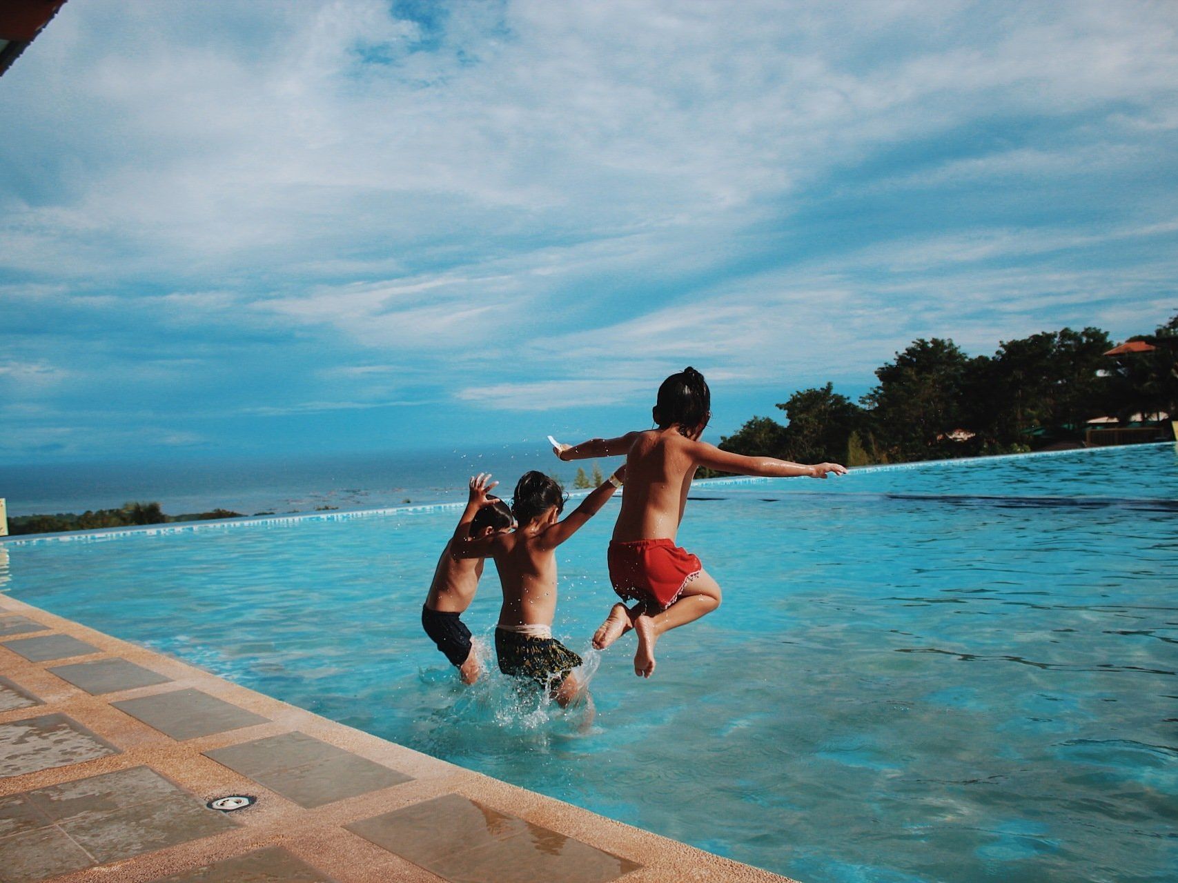 Three young boys are jumping into a swimming pool.