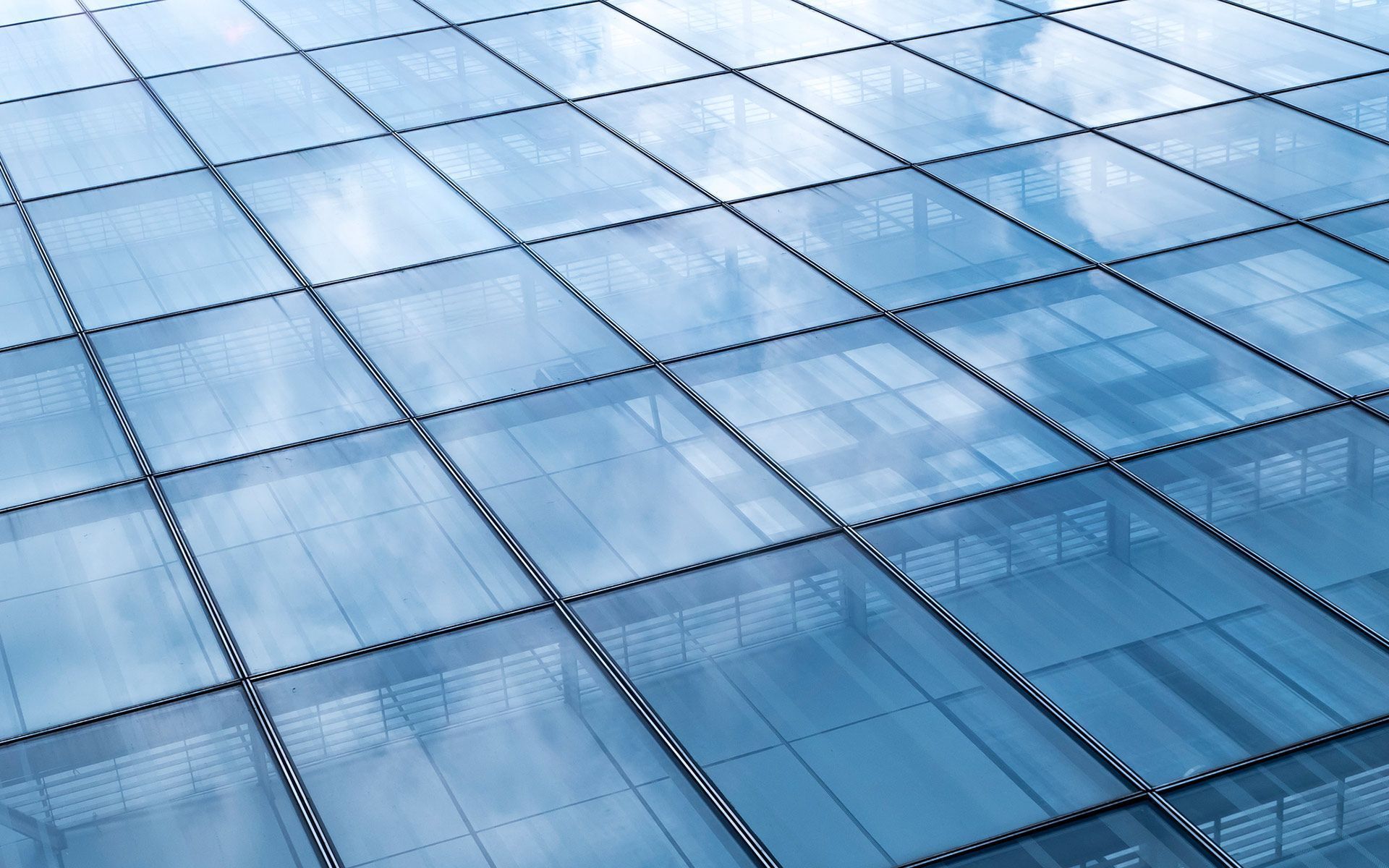 Glass building facade reflecting a cloudy blue sky. Square paneled structure.