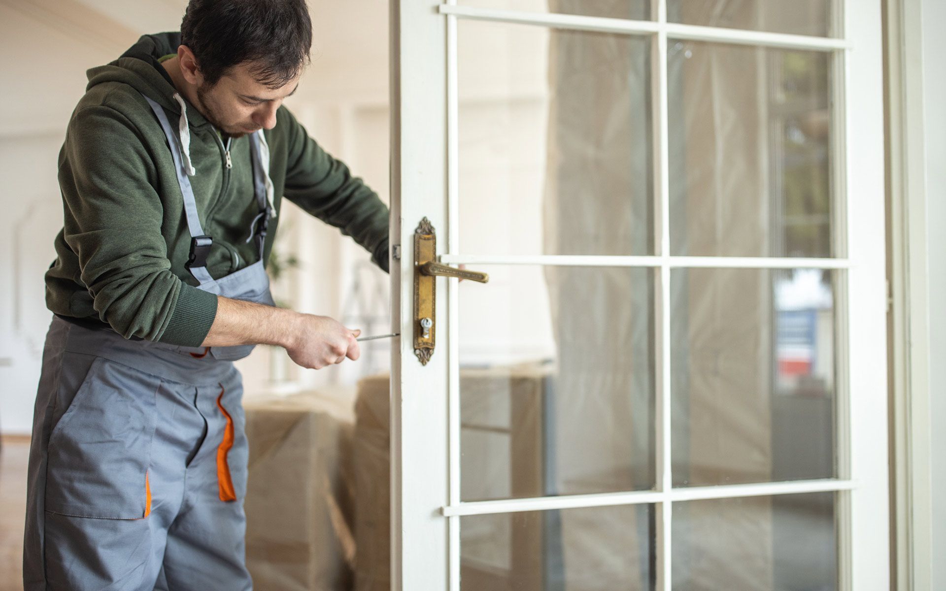 Person in gray overalls repairs a door's handle with a screwdriver.