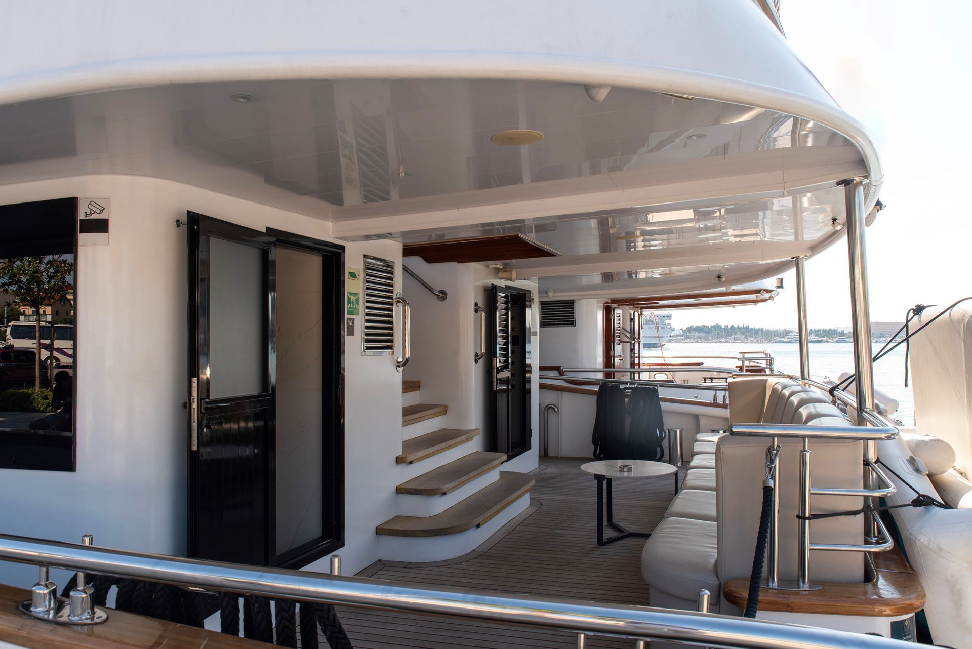 Exterior deck of a luxury yacht with white walls, sliding doors, stairs, and seating.