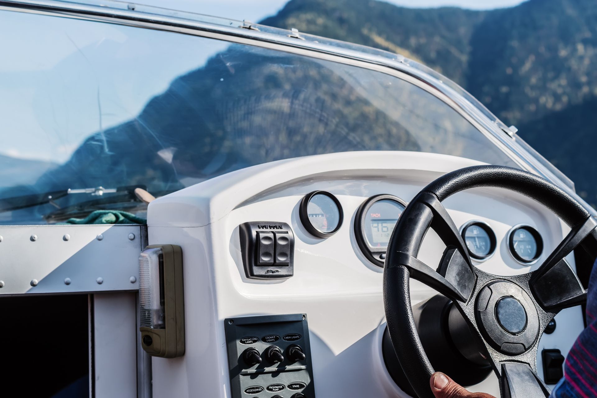 Boat dashboard with steering wheel and gauges. Mountains in background.