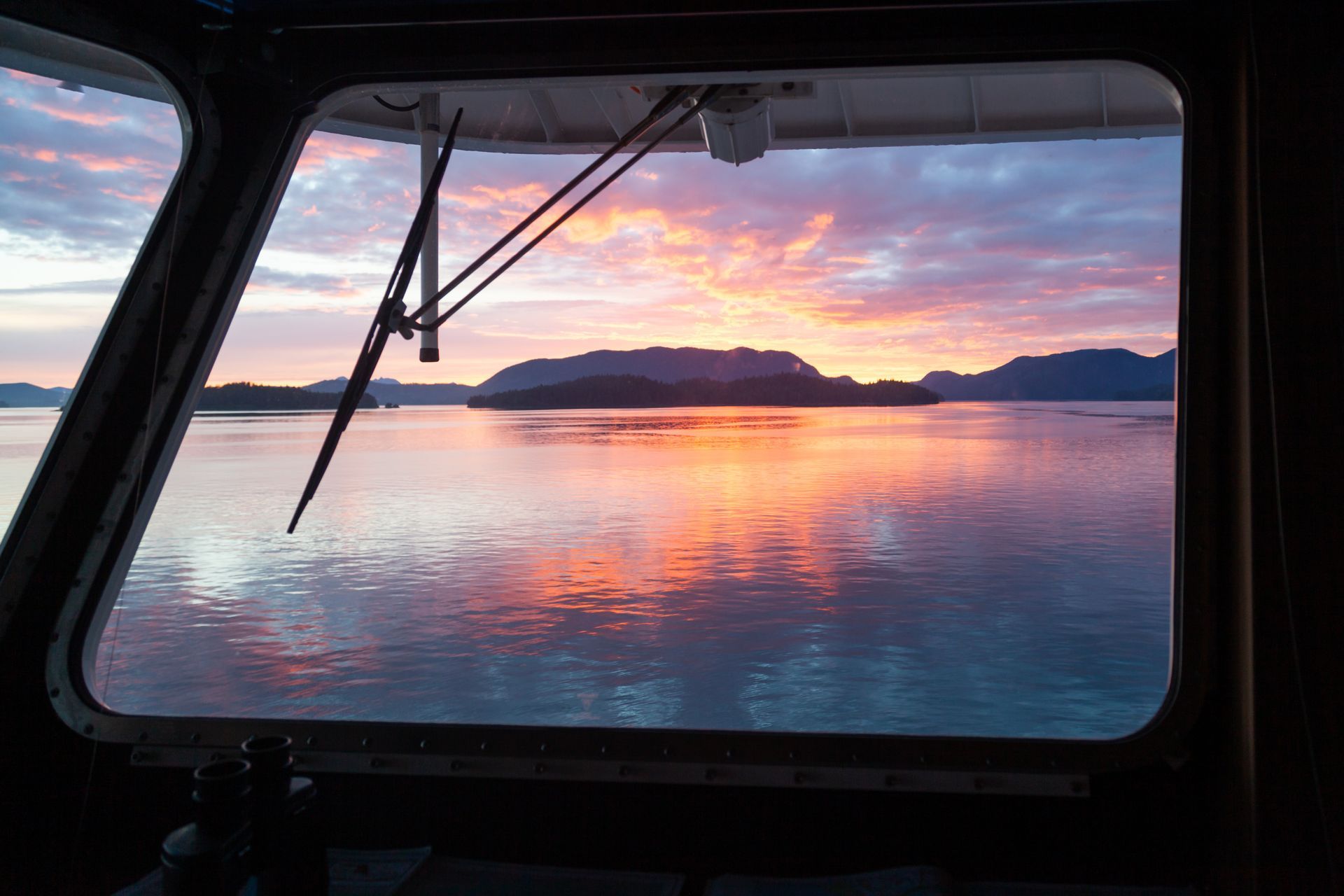Sunrise over water, viewed from a boat window; orange and pink sky reflects on calm water.