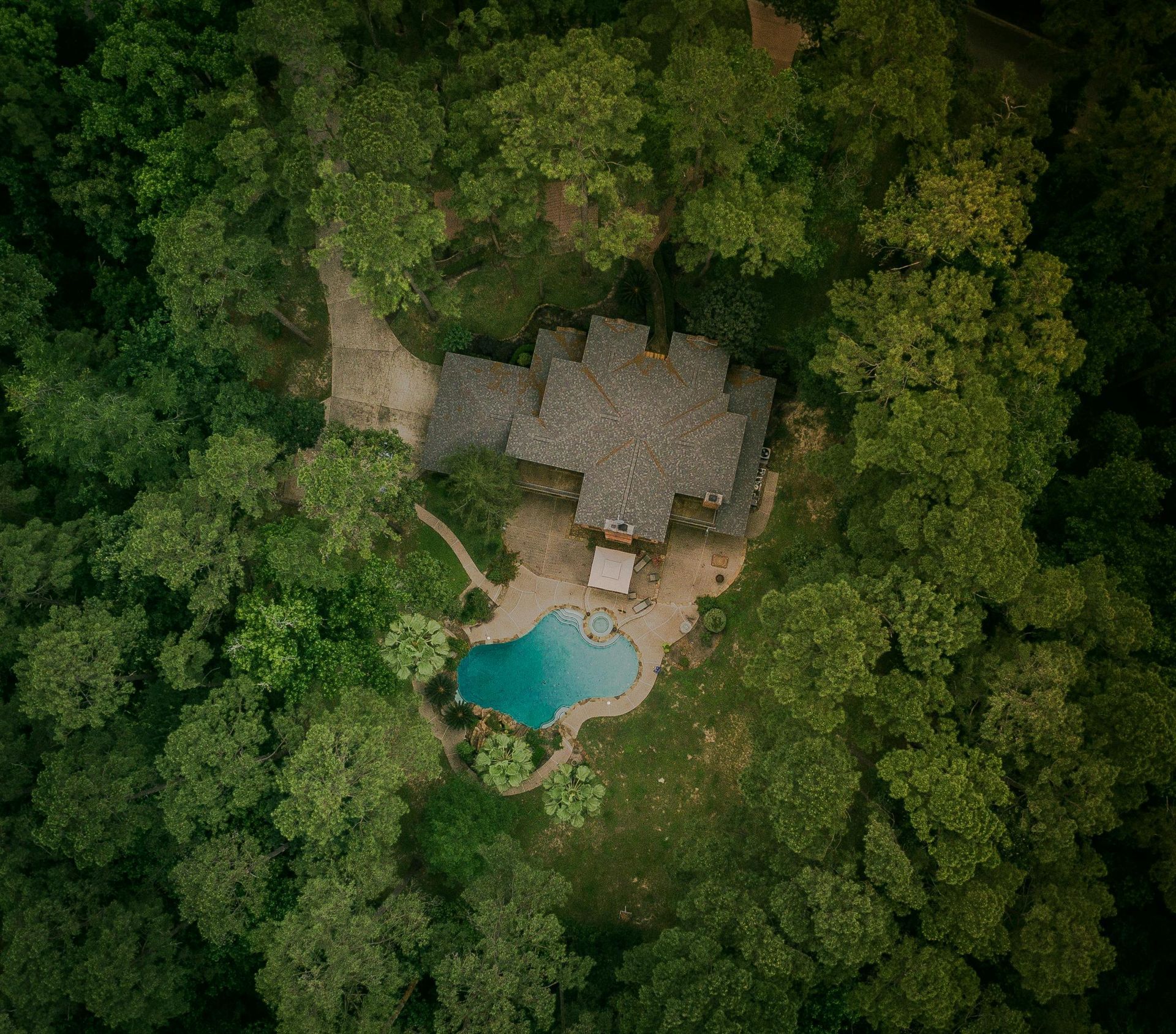 An aerial view of a house with a pool in the middle of a forest.