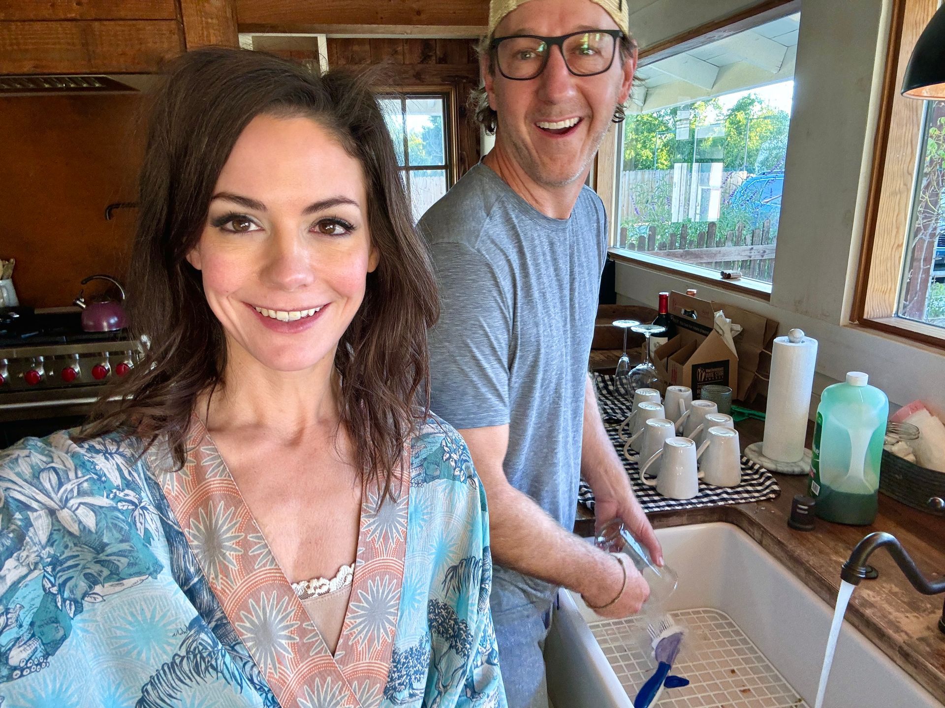 Woman smiles at camera while man washes dishes in a kitchen.