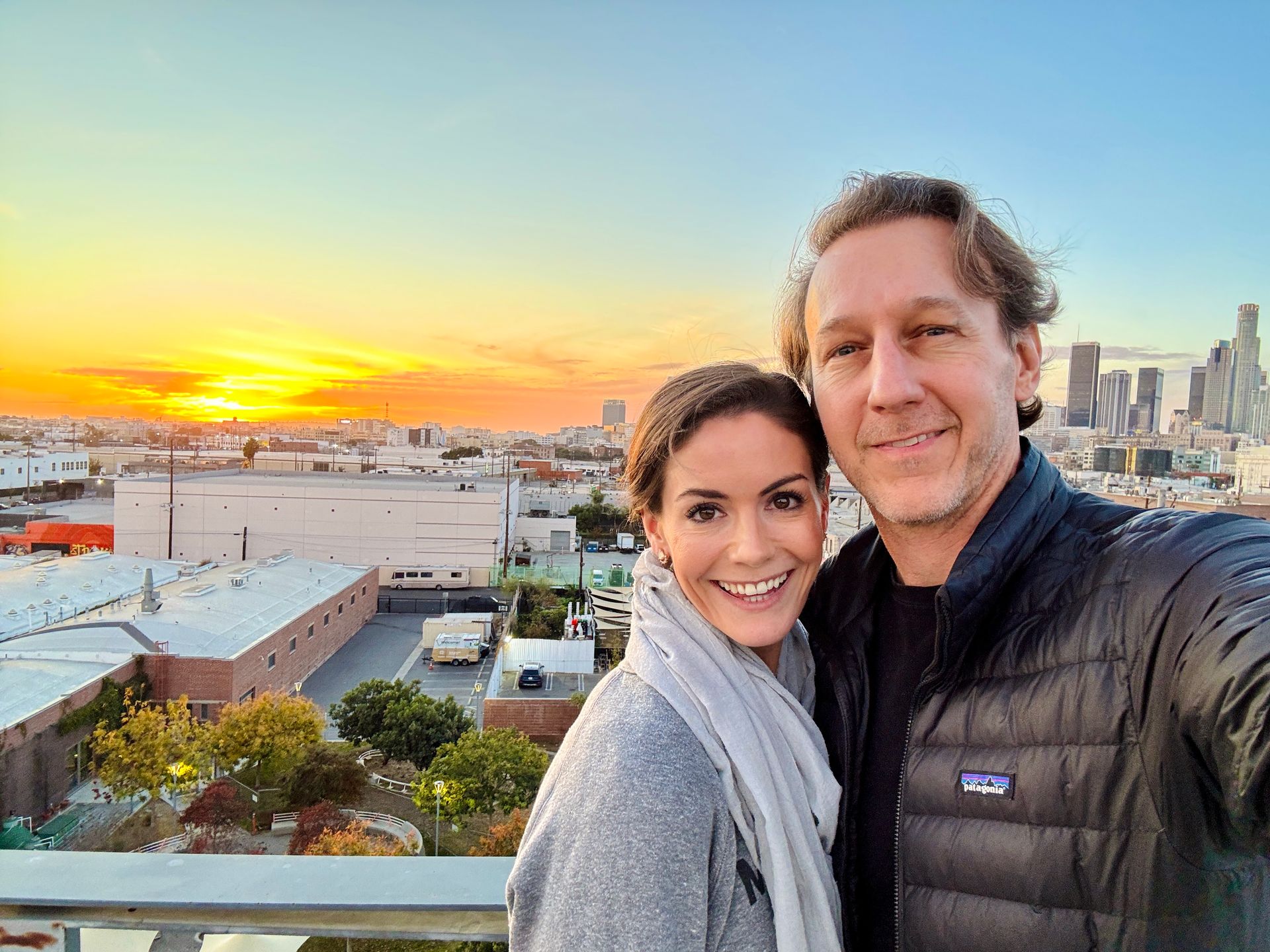 Woman and man in white robes smiling, taking a selfie near a window.
