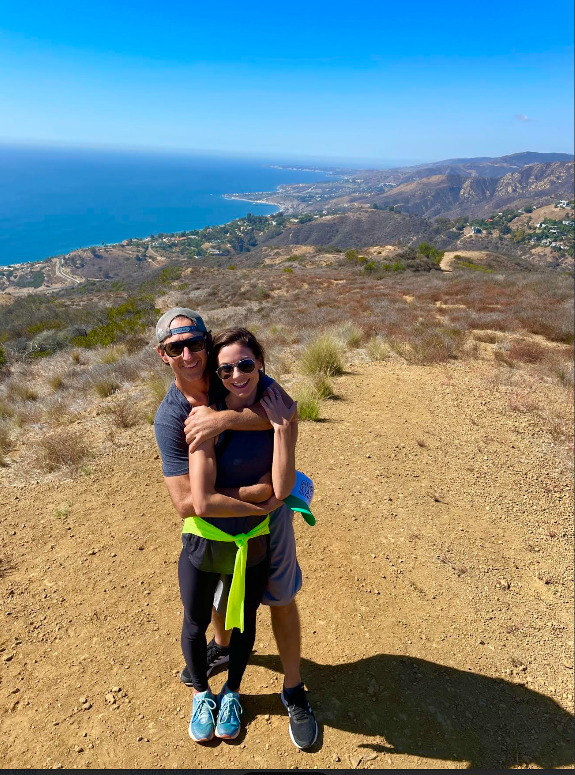 Couple dancing at an outdoor wedding reception. Bride in white gown, groom in a suit, with string lights overhead.