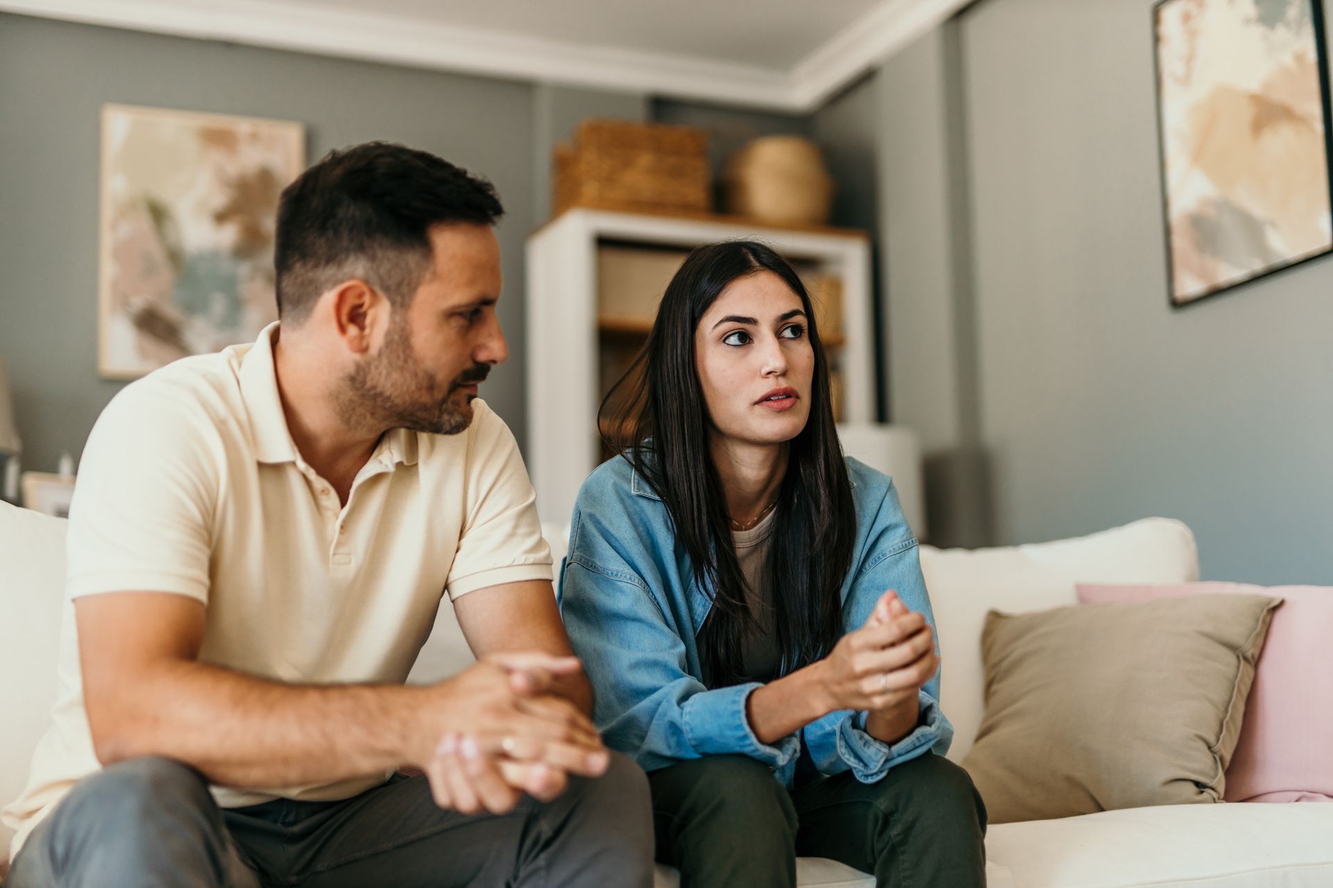 A man and woman sit on a sofa, talking. The woman looks concerned; the man listens.