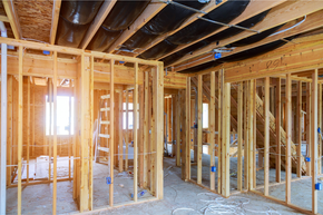 Interior view of a building under construction, showing wooden framing of walls, electrical boxes, and ductwork.