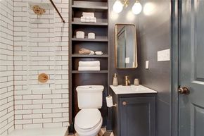 Bathroom with a dark gray vanity and shelves, white subway tile shower, and brass fixtures.