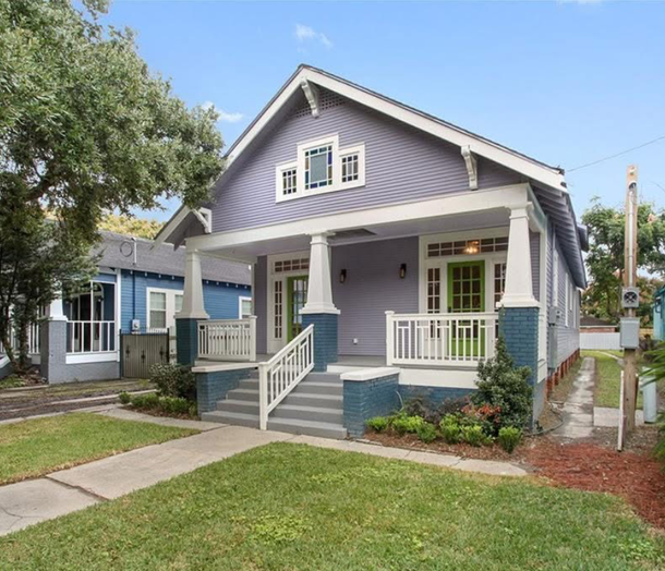 A light purple craftsman house with a front porch, green front door, and blue accents, set on a green lawn.