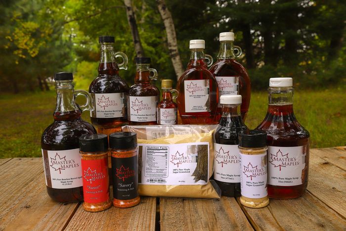 eight bottles of syrup, two seasonings, one sugar shaker and a bag of sugar, all on top of a barrel