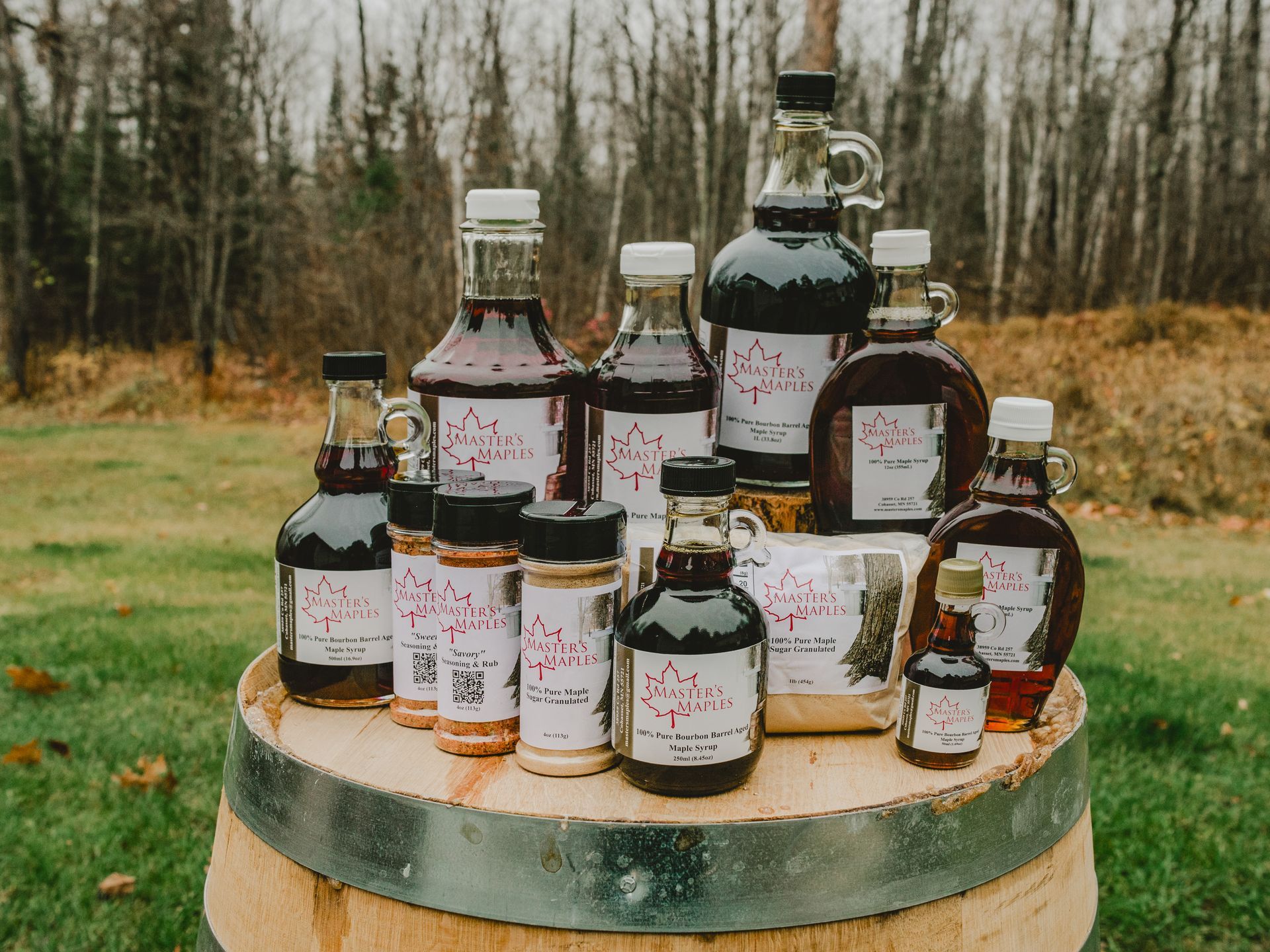 eight bottles of syrup, two seasonings, one sugar shaker and a bag of sugar, all on top of a barrel