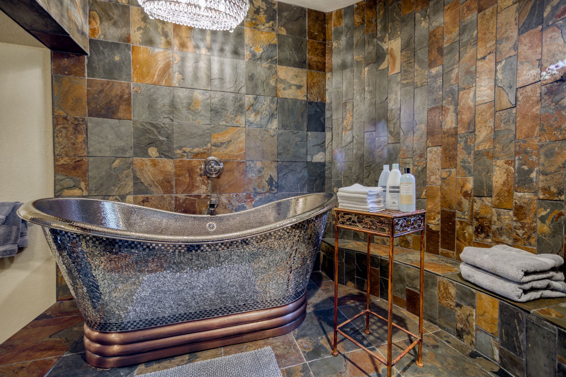 A bathroom with a copper bathtub and slate tiles.