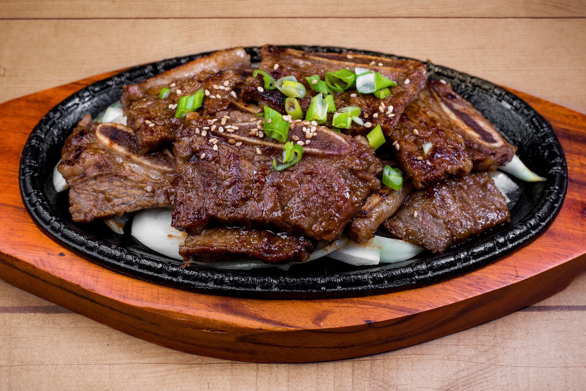 A sizzling plate of meat and onions on a wooden table.