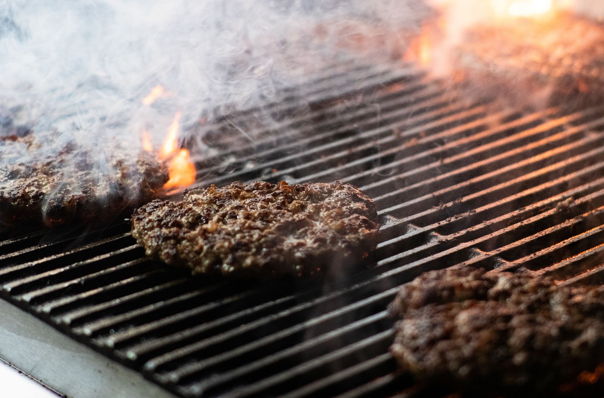 Hamburgers are cooking on a grill with flames and smoke coming out of it.