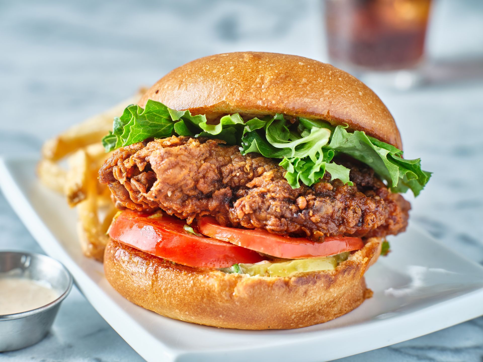 A fried chicken sandwich with lettuce , tomato , and french fries on a white plate.