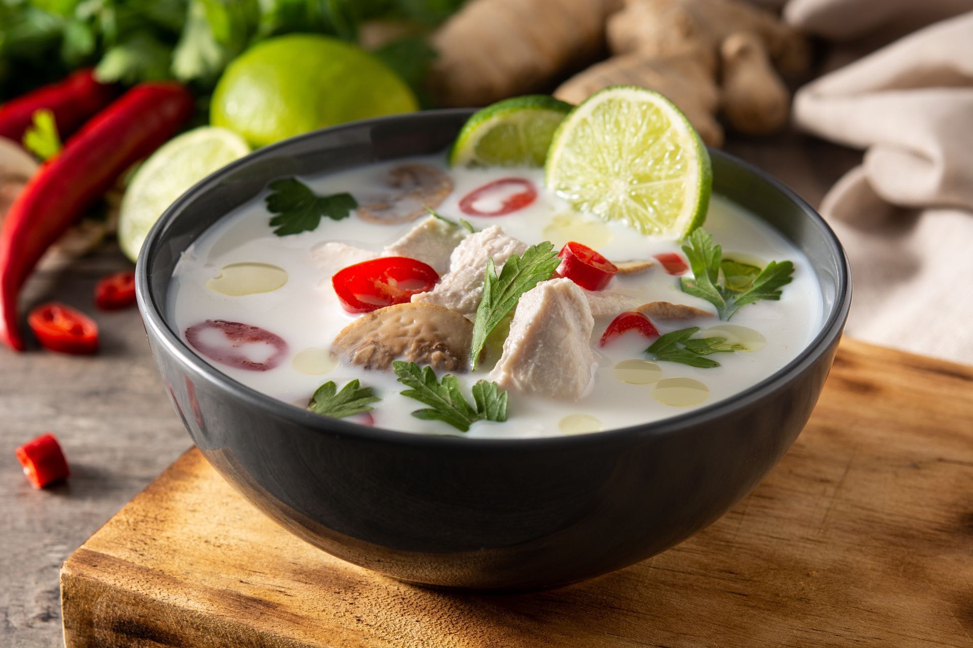 A bowl of soup with chicken and limes on a wooden table.