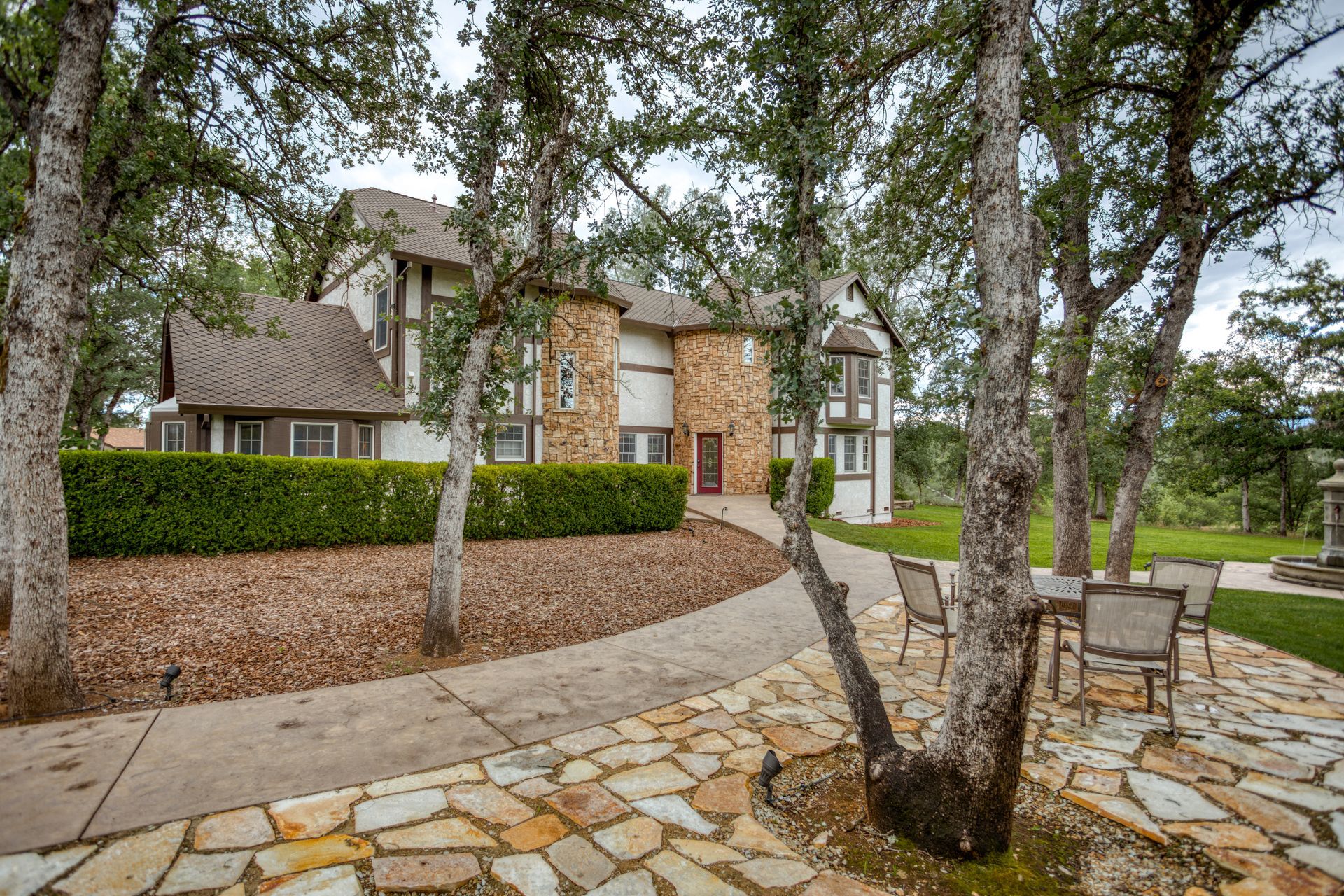 A large house is surrounded by trees and a stone walkway.