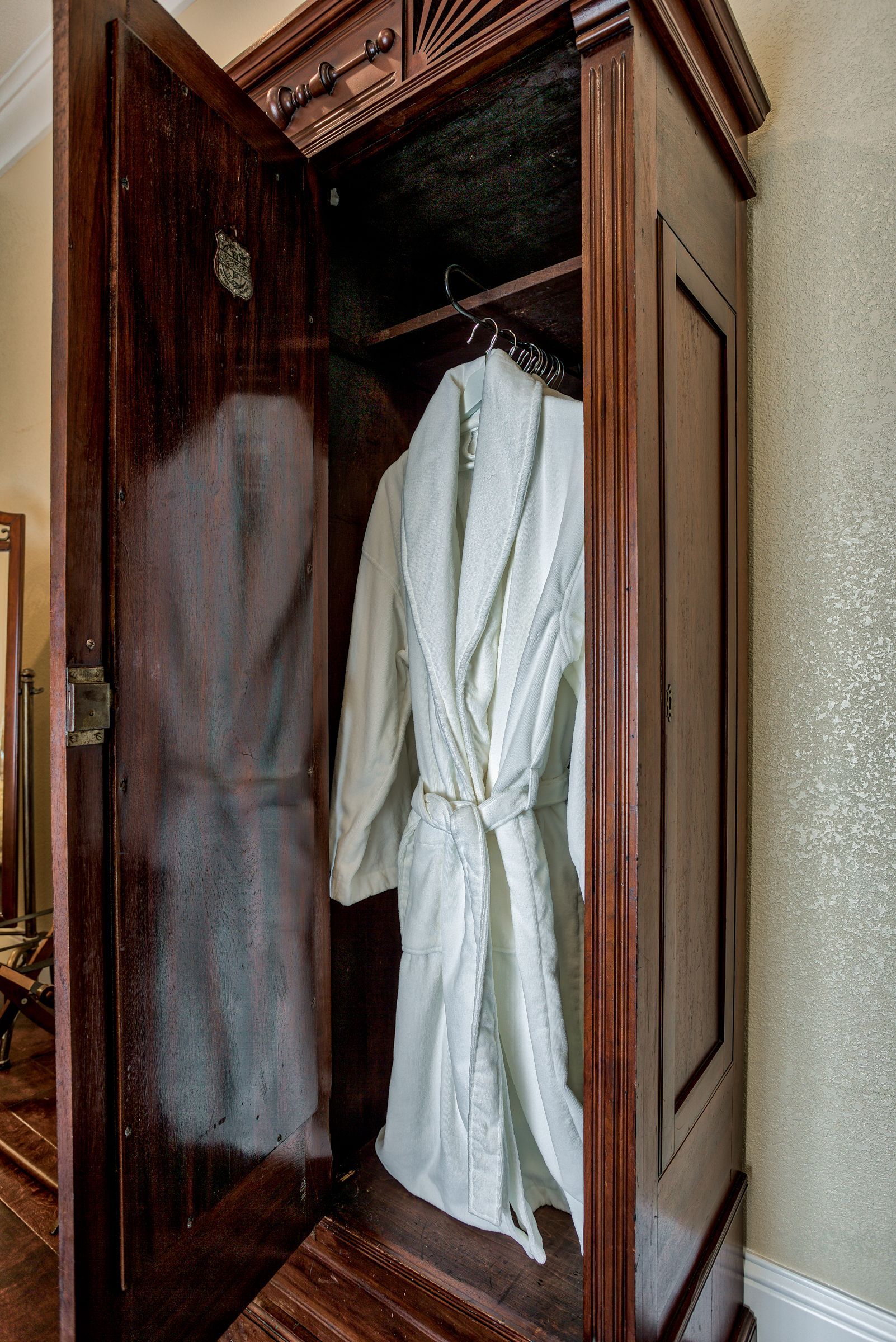 A white robe is hanging in a wooden wardrobe.