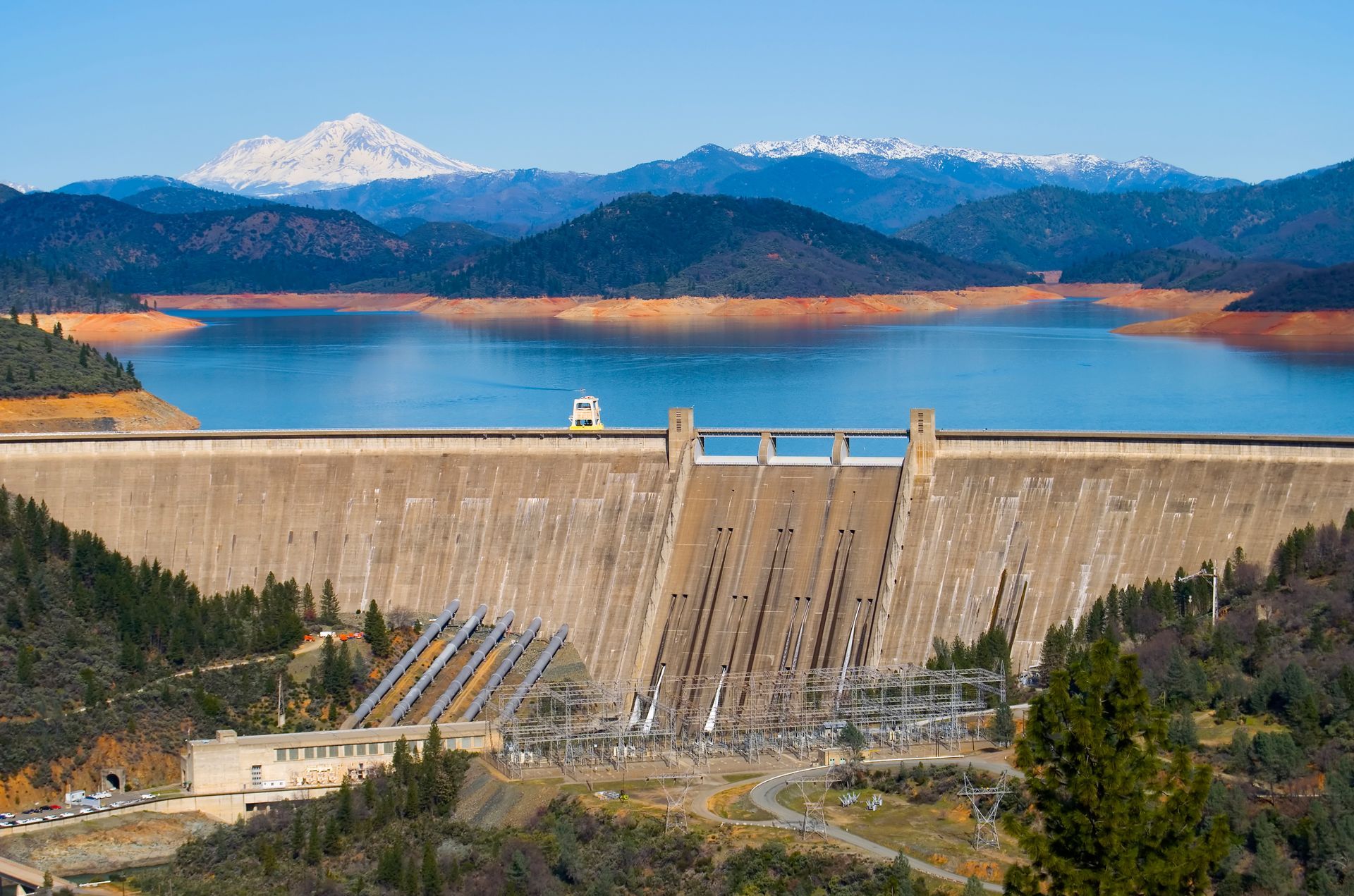 A large dam surrounded by mountains and trees with a lake in the background.