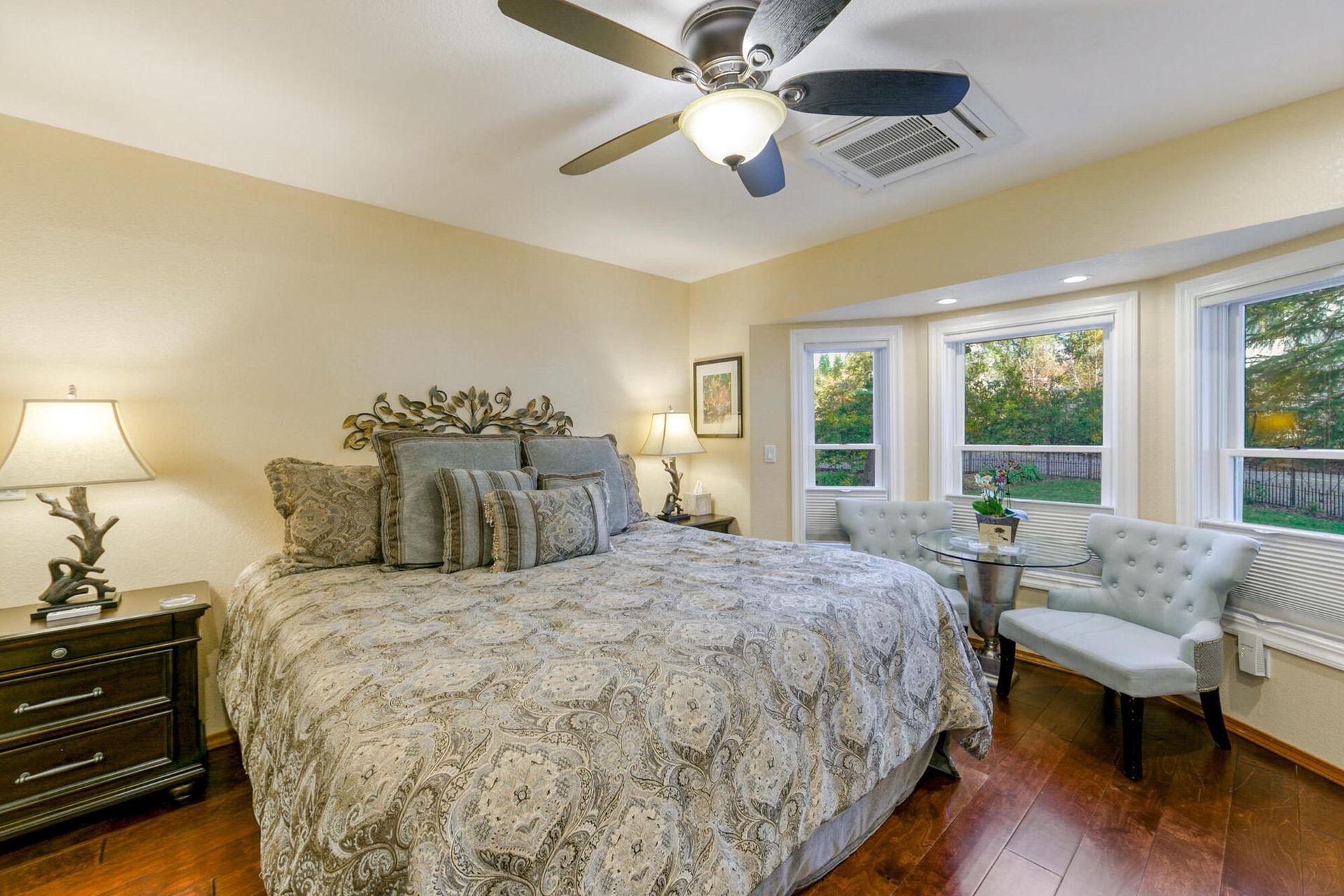 A bedroom with a king size bed , chairs , lamps , and a ceiling fan.