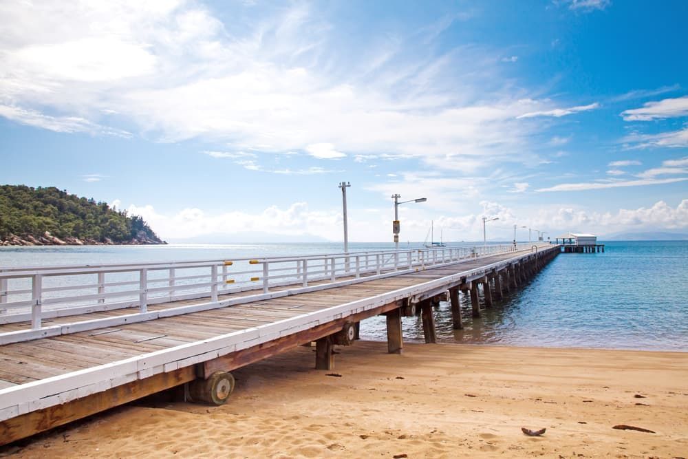Scenic View of a Lengthy Timber Jetty With a White Railing Extending Over Tranquil Waters - Tree Services in Townsville, QLD