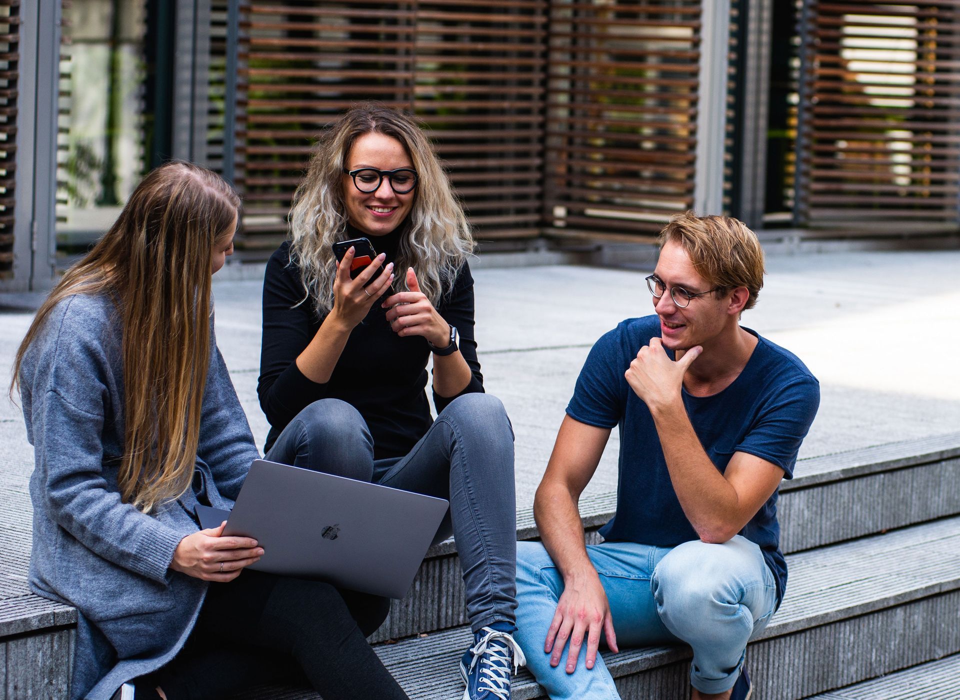 Three young work employees are talking about corporate wellness and are sitting on steps in front of their office building.