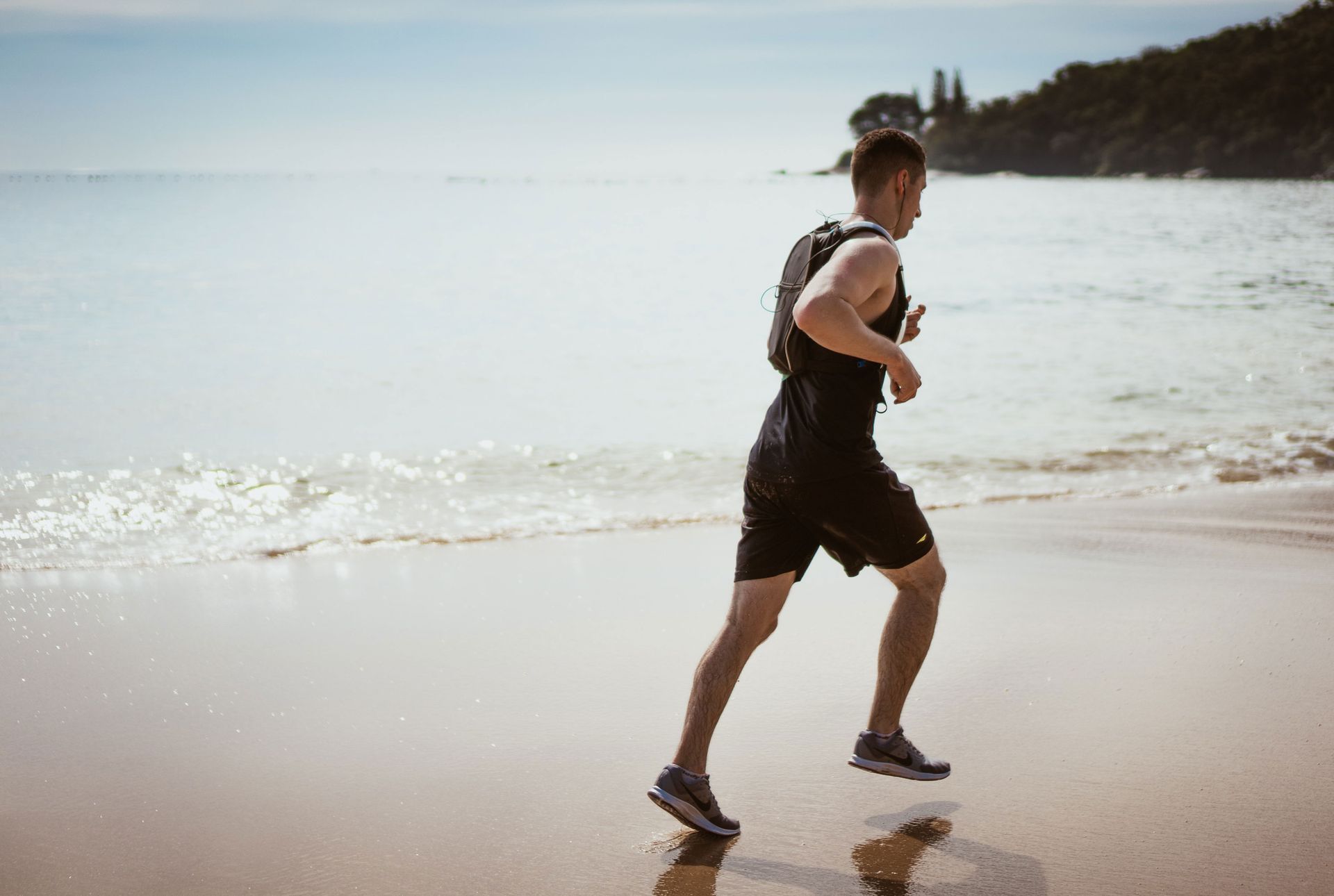 A man trying to improve his mental and physical well-being by running on the beach on a sunny day.
