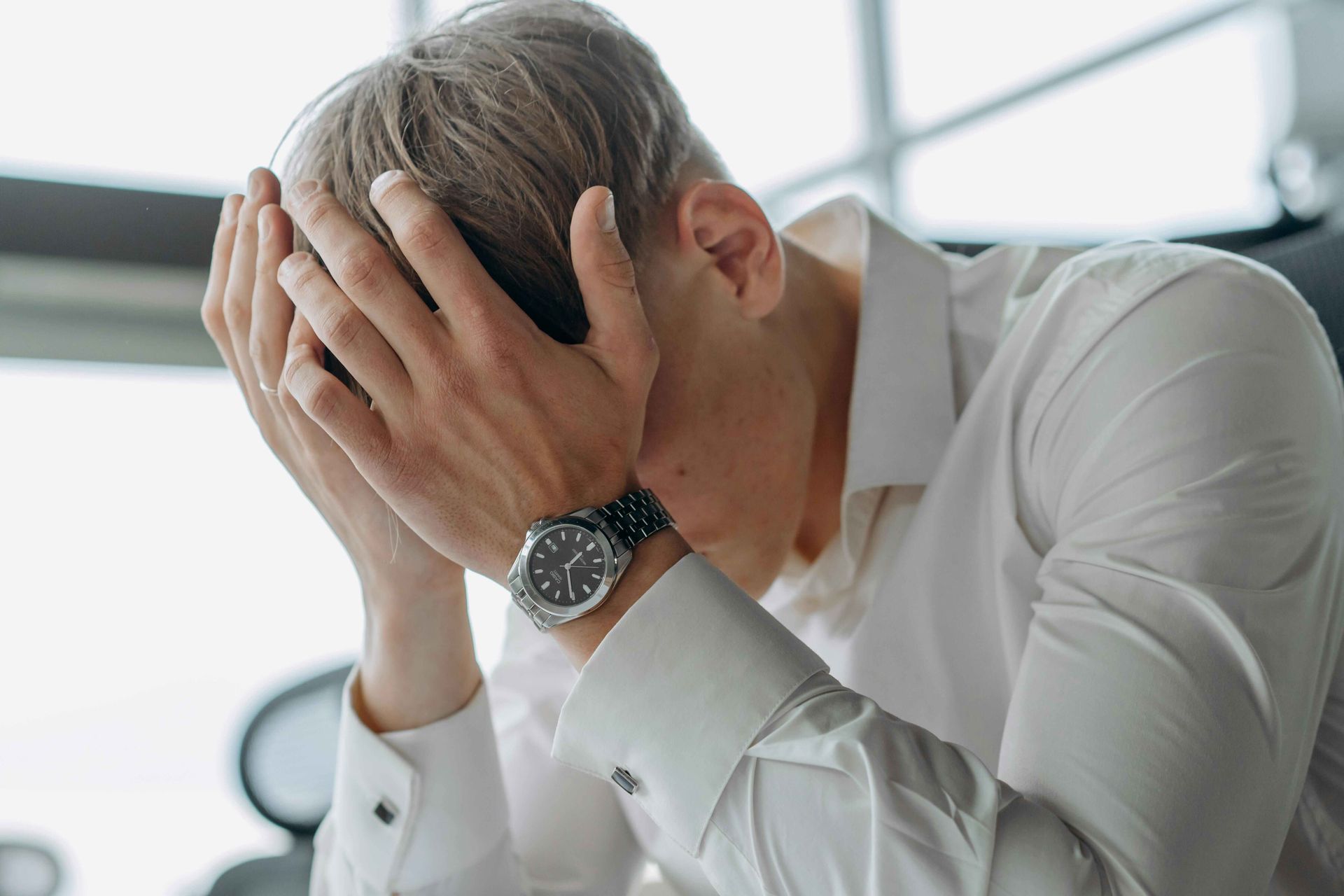 A male corporate executive struggling with work pressure. He's holding his head in his hands.