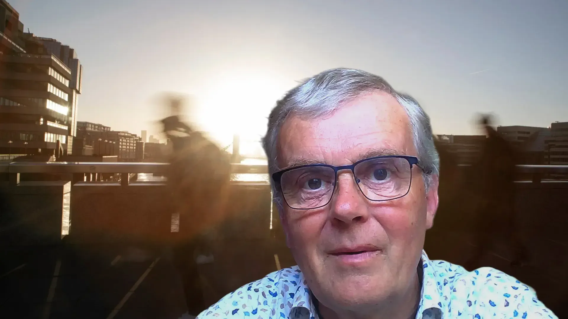 Man met bril voor een wazig stadsgezicht bij zonsondergang.