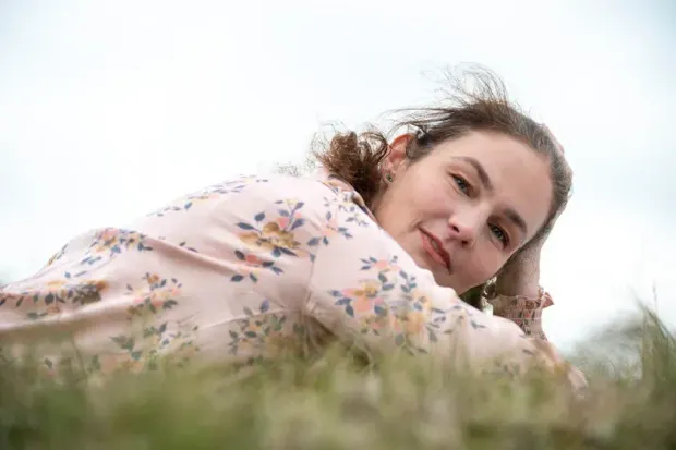 Annemarie in bloemenblouse ligt in het gras en kijkt naar de camera.