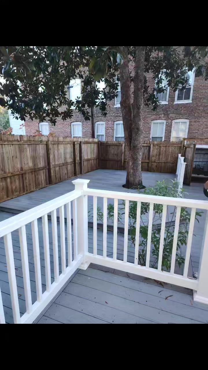 A deck with a white railing and a wooden fence in the backyard of a house.