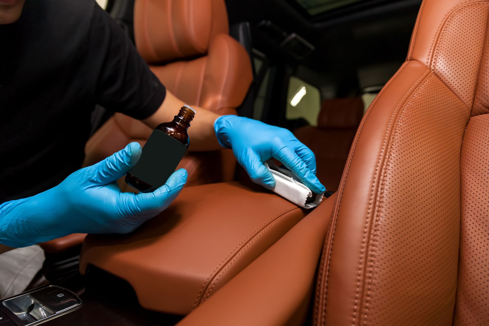 A man wearing blue gloves is cleaning the seats of a car.