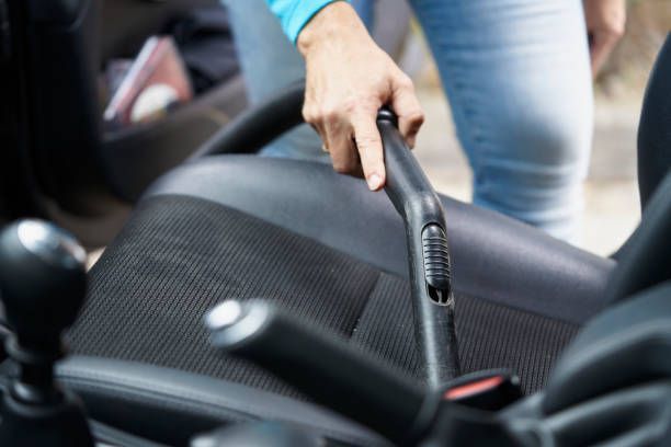 A woman is cleaning the seats of a car with a vacuum cleaner.