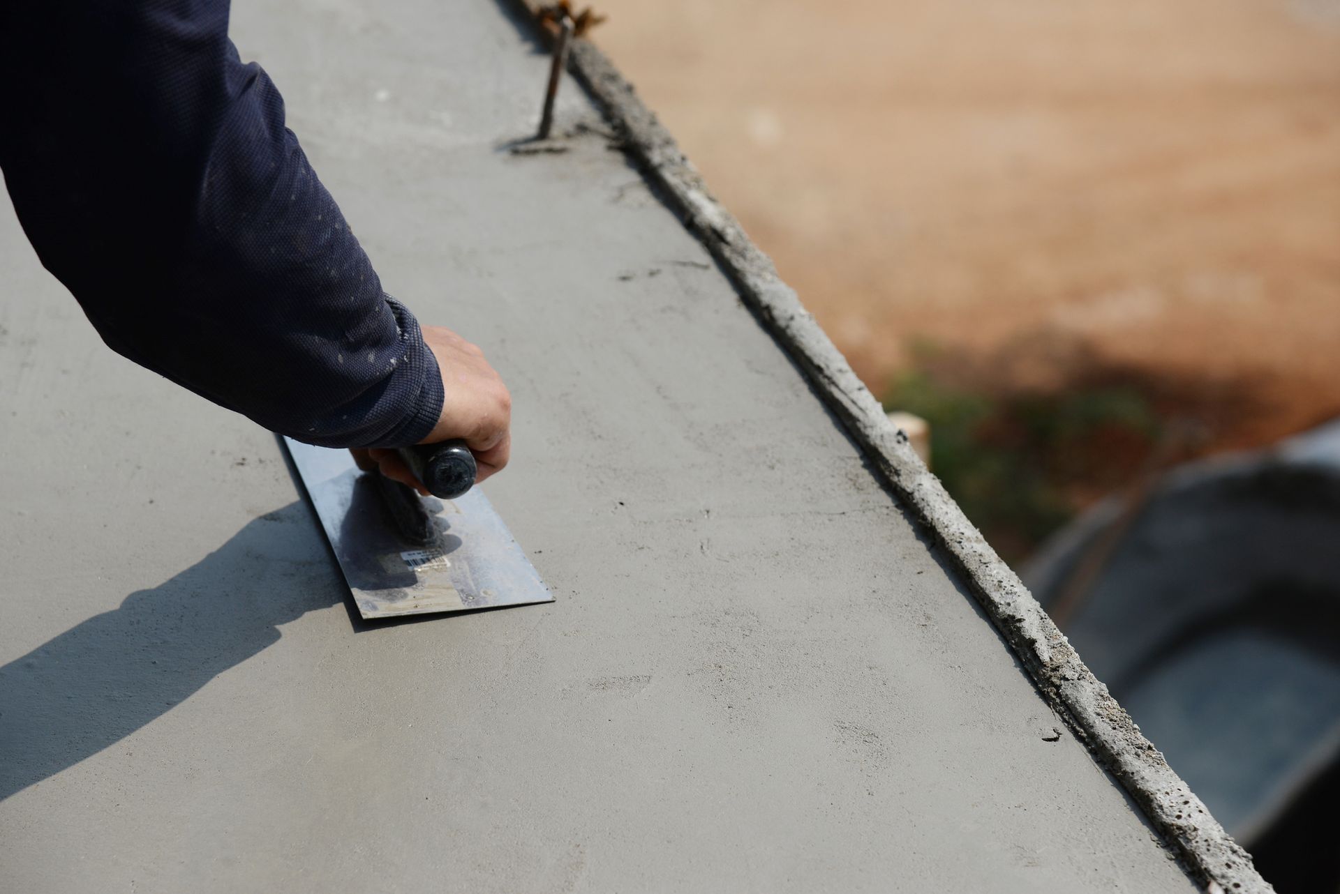 A person is using a trowel to spread concrete on a roof.