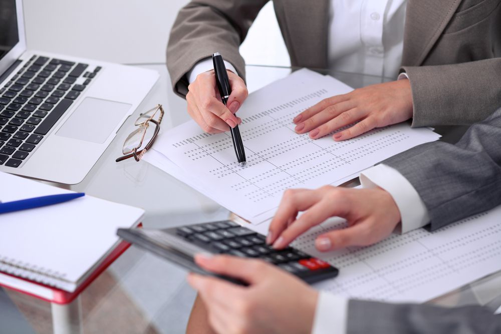 Two people in business suits reviewing documents and using a calculator at a desk — All Finanz & Insurance Solutions Mackay in Cannovale, QLD