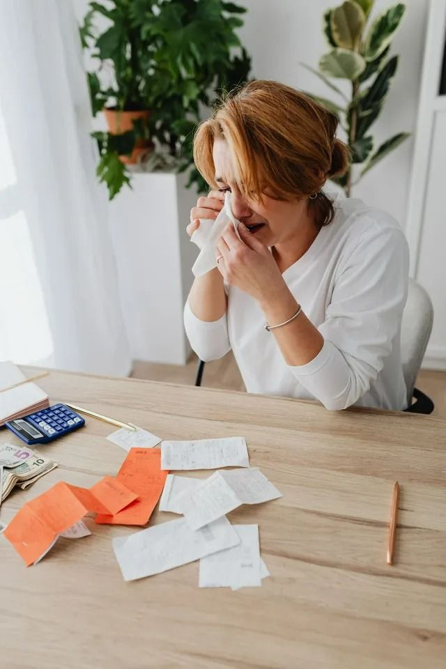 Woman Blowing Nose at Desk with Bills and Calculator — All Finanz & Insurance Solutions Mackay in North Mackay, QLD