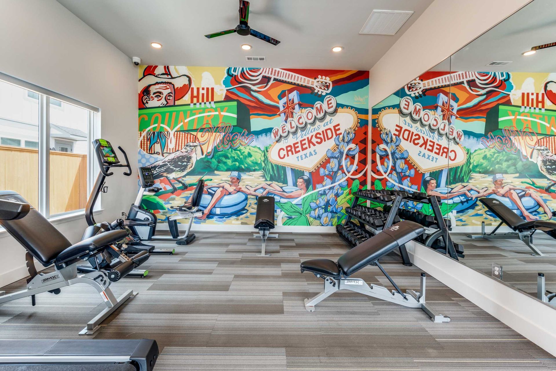 Gym interior with colorful mural, exercise equipment, and large mirror.