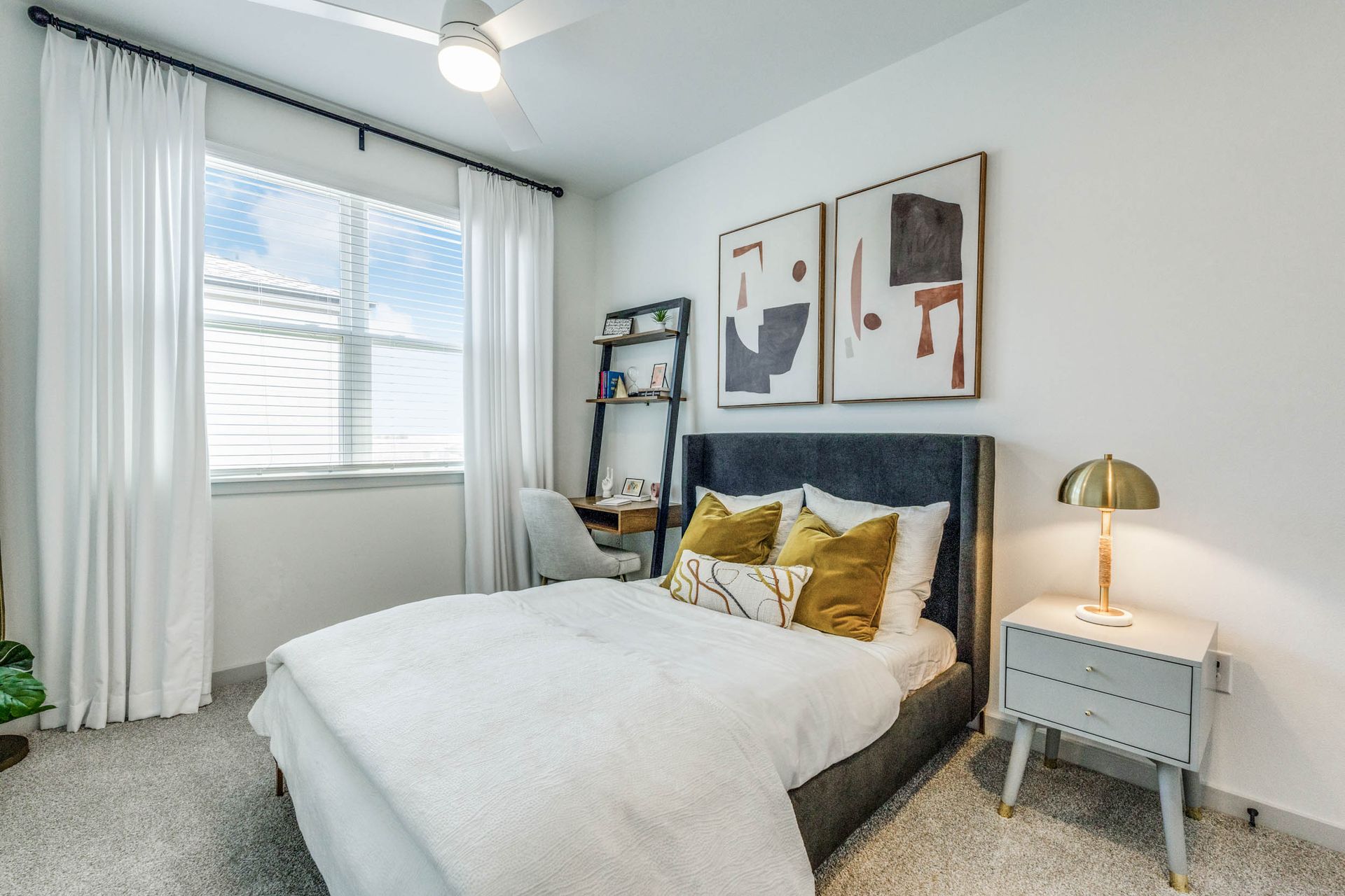 Cozy bedroom featuring a bed with decorative pillows, modern artwork, and a small desk.