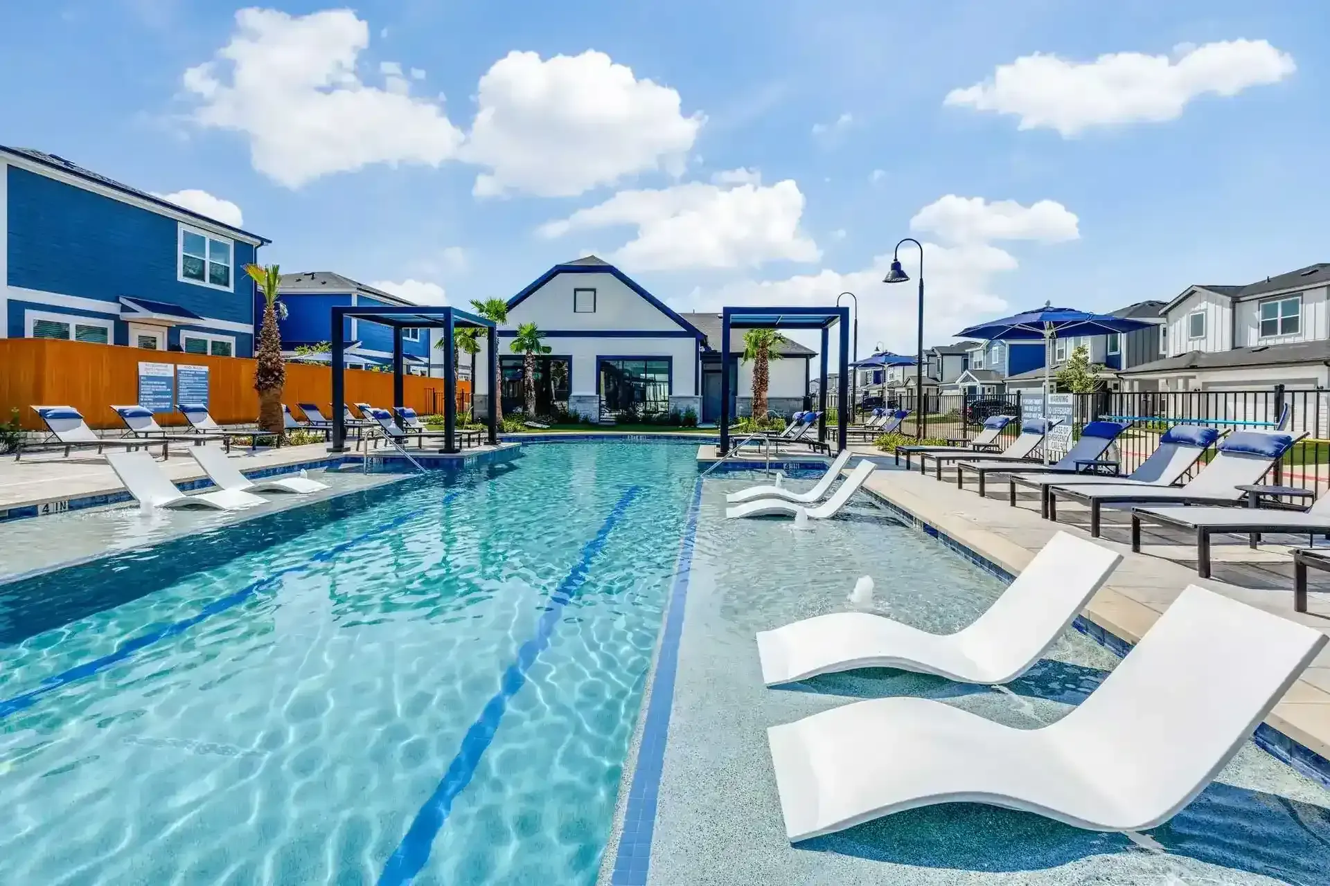A bright community pool area with lounge chairs and blue umbrellas.