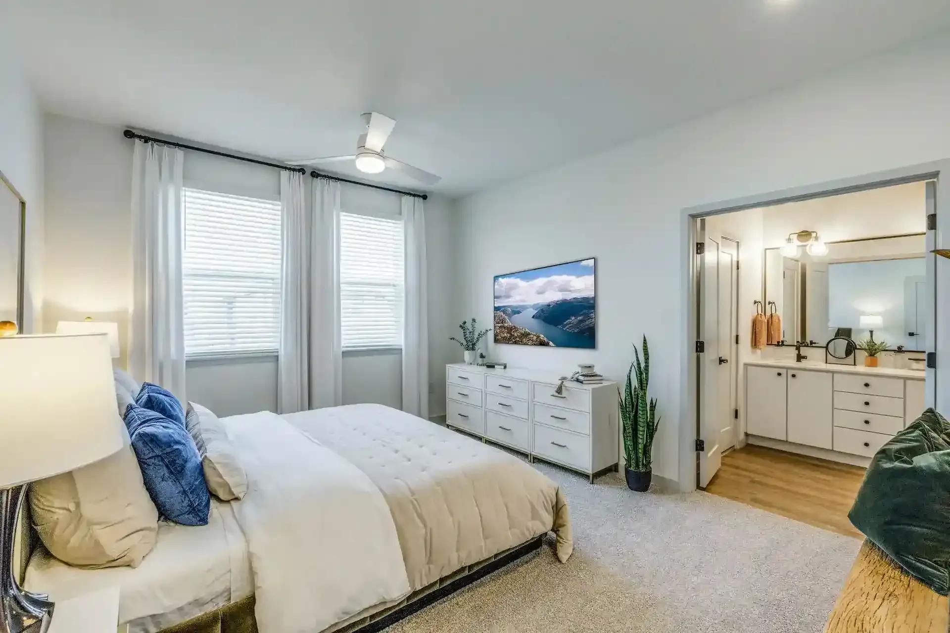 A modern bedroom with a bed, decorative pillows, a dresser, and an adjoining bathroom.