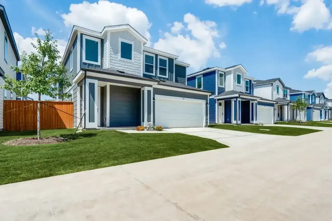 Row of modern houses with garages and green lawns under a blue sky