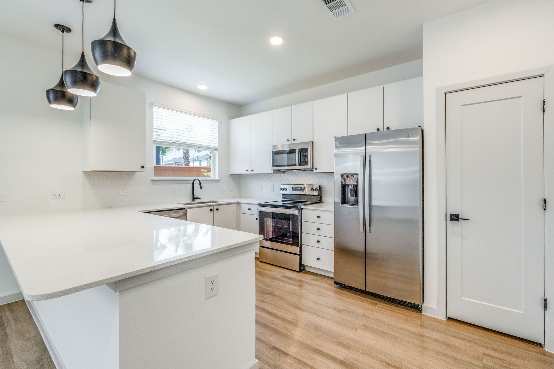 Modern white kitchen with stainless steel appliances, island, and pendant lights.